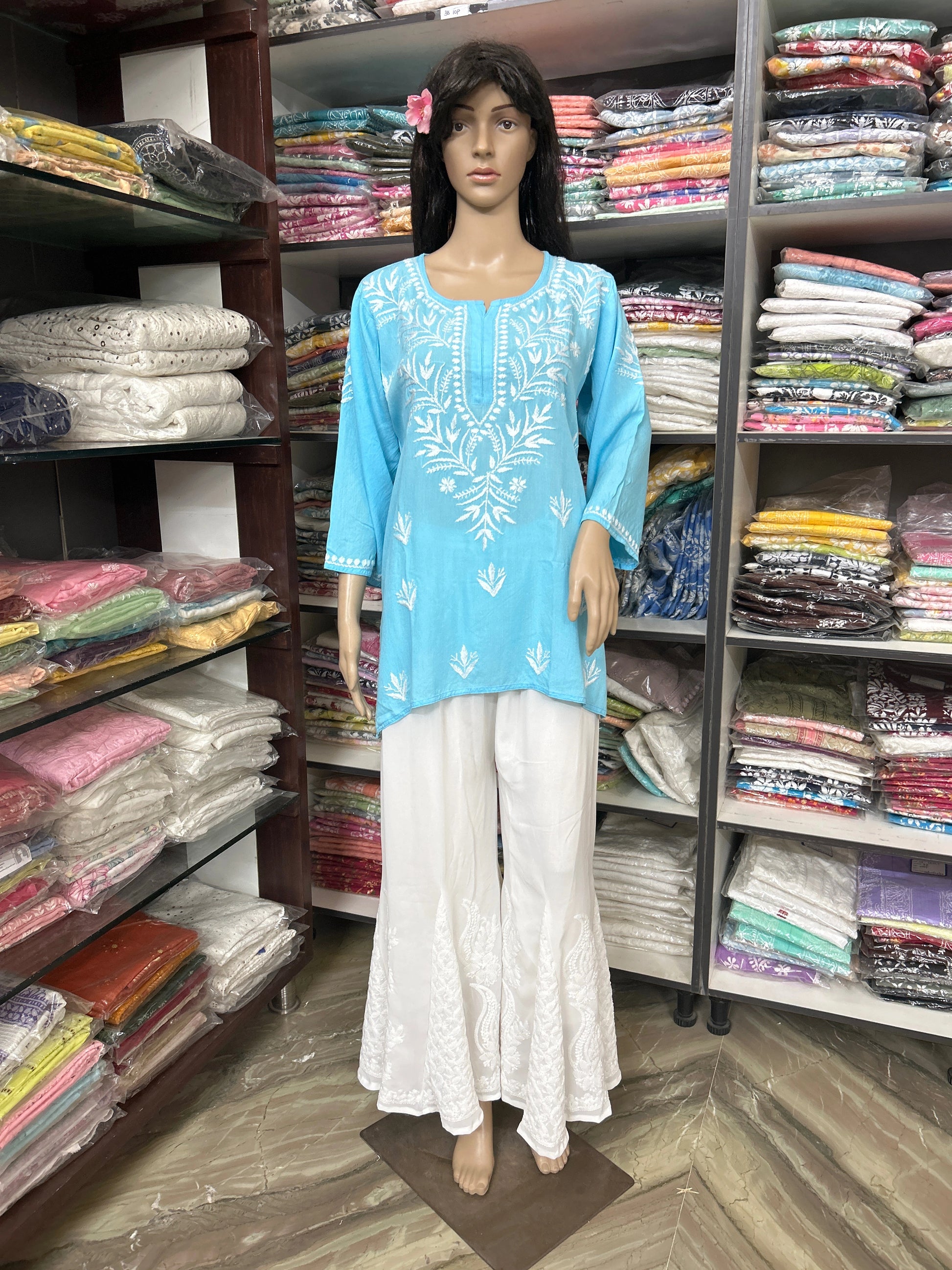 Mannequin wearing a blue embroidered top and white pants in a fabric store.