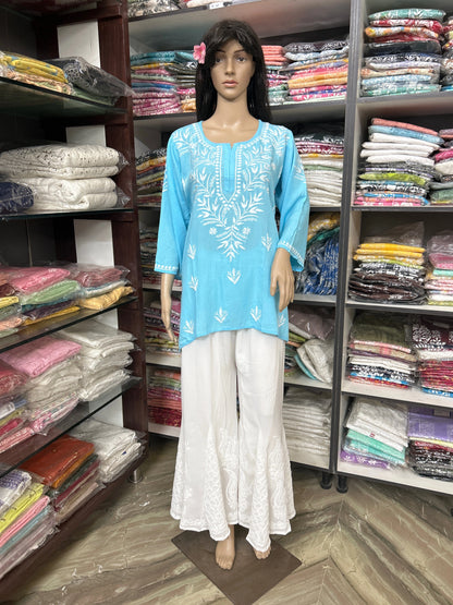 Mannequin wearing a blue embroidered top and white pants in a fabric store.