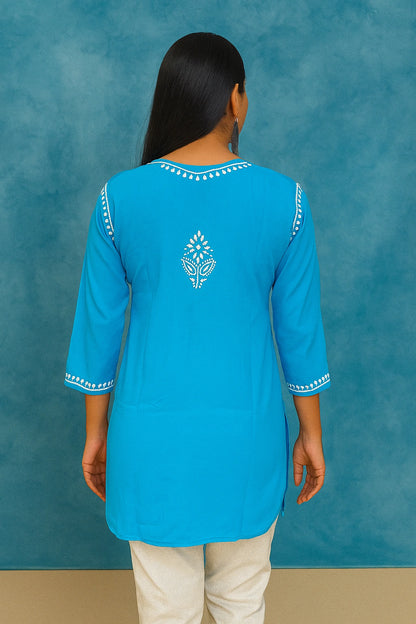 Woman wearing a lucknowi chikankari blue top with white polka dots and blue jeans on a gray background