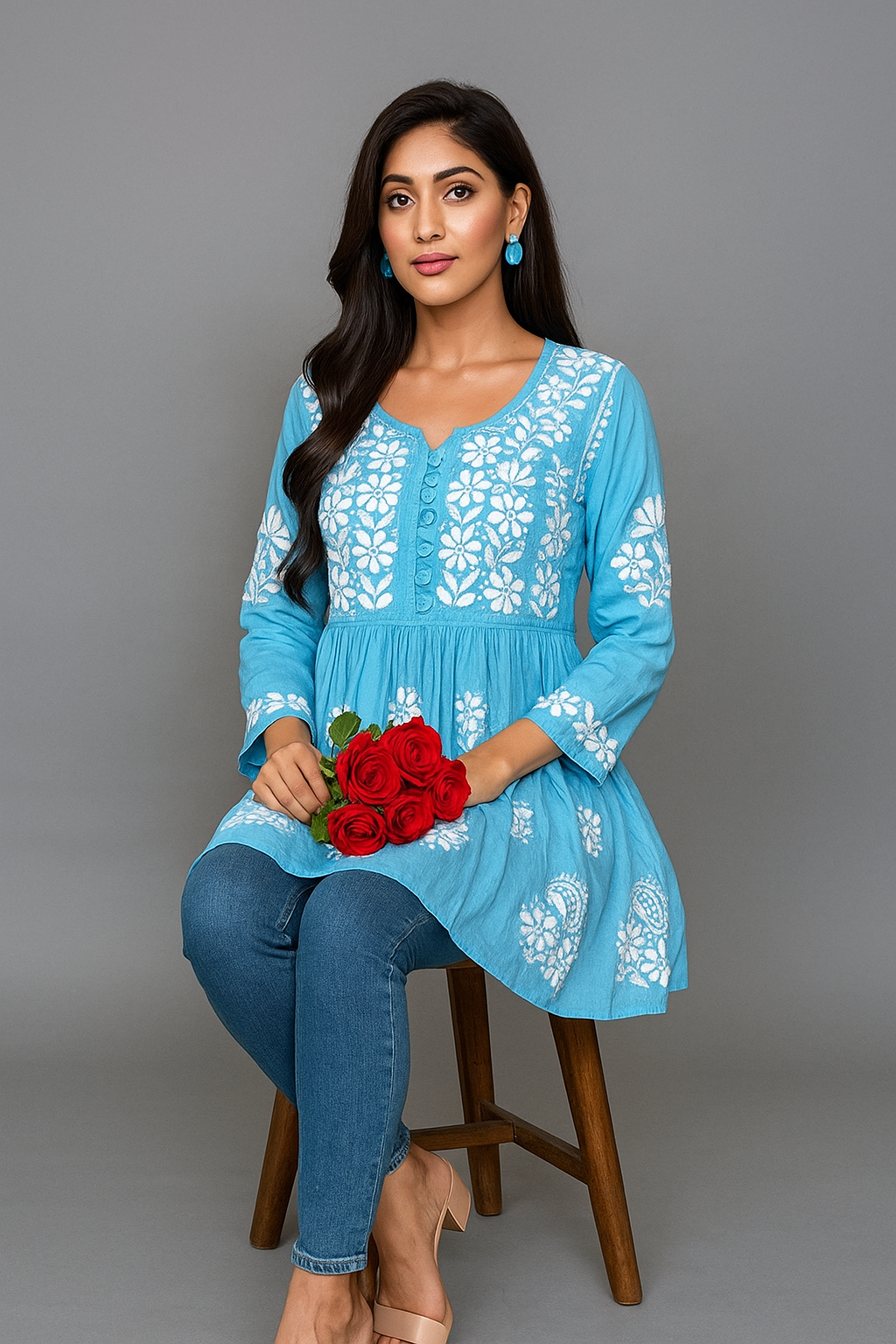 Woman wearing a blue embroidered top and jeans, holding red flowers on a gray background
