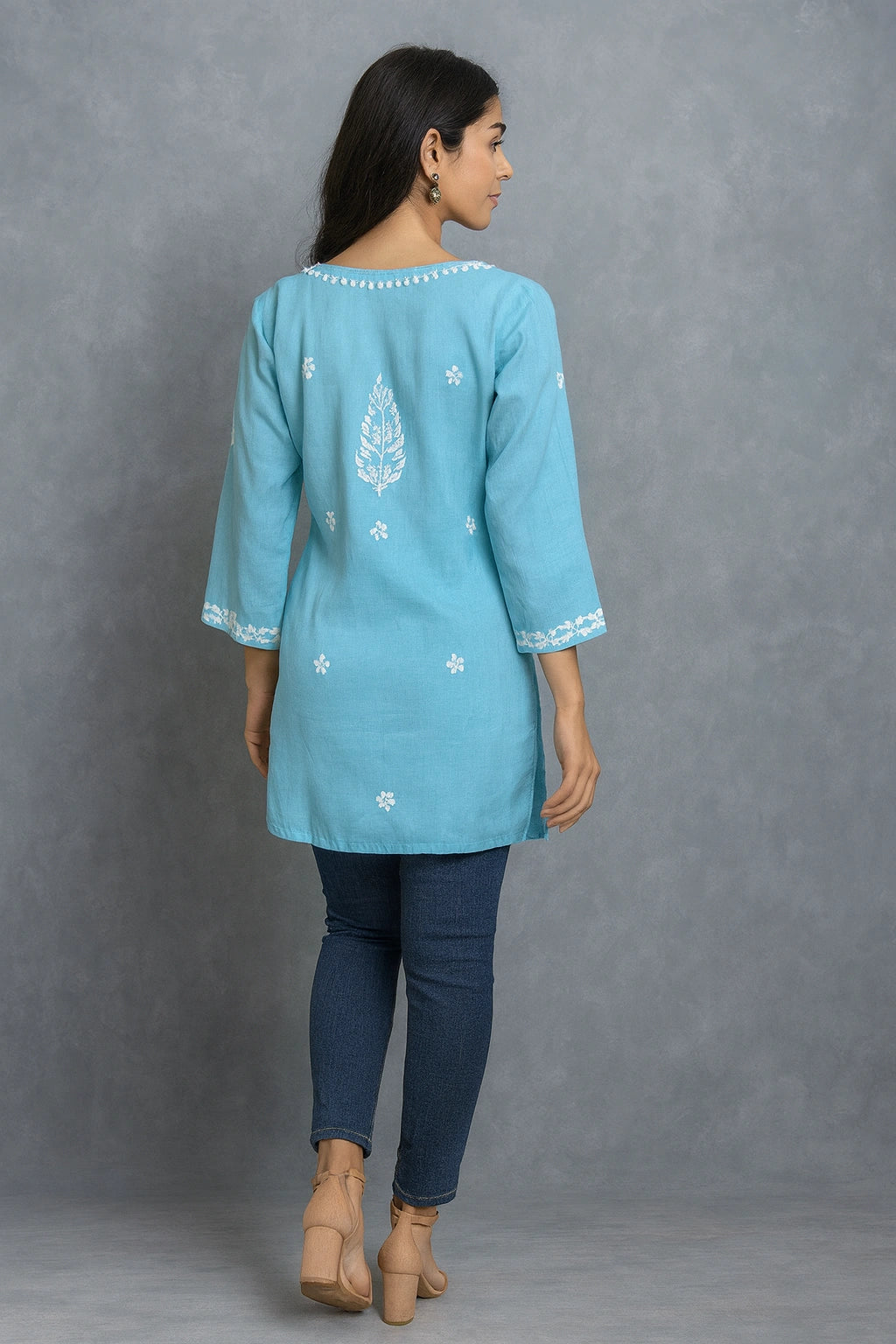 Woman wearing a lucknowi chikankari blue top with white polka dots and blue jeans on a gray background