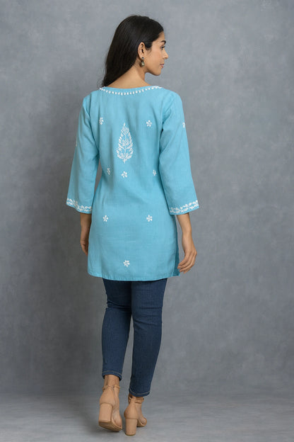 Woman wearing a lucknowi chikankari blue top with white polka dots and blue jeans on a gray background