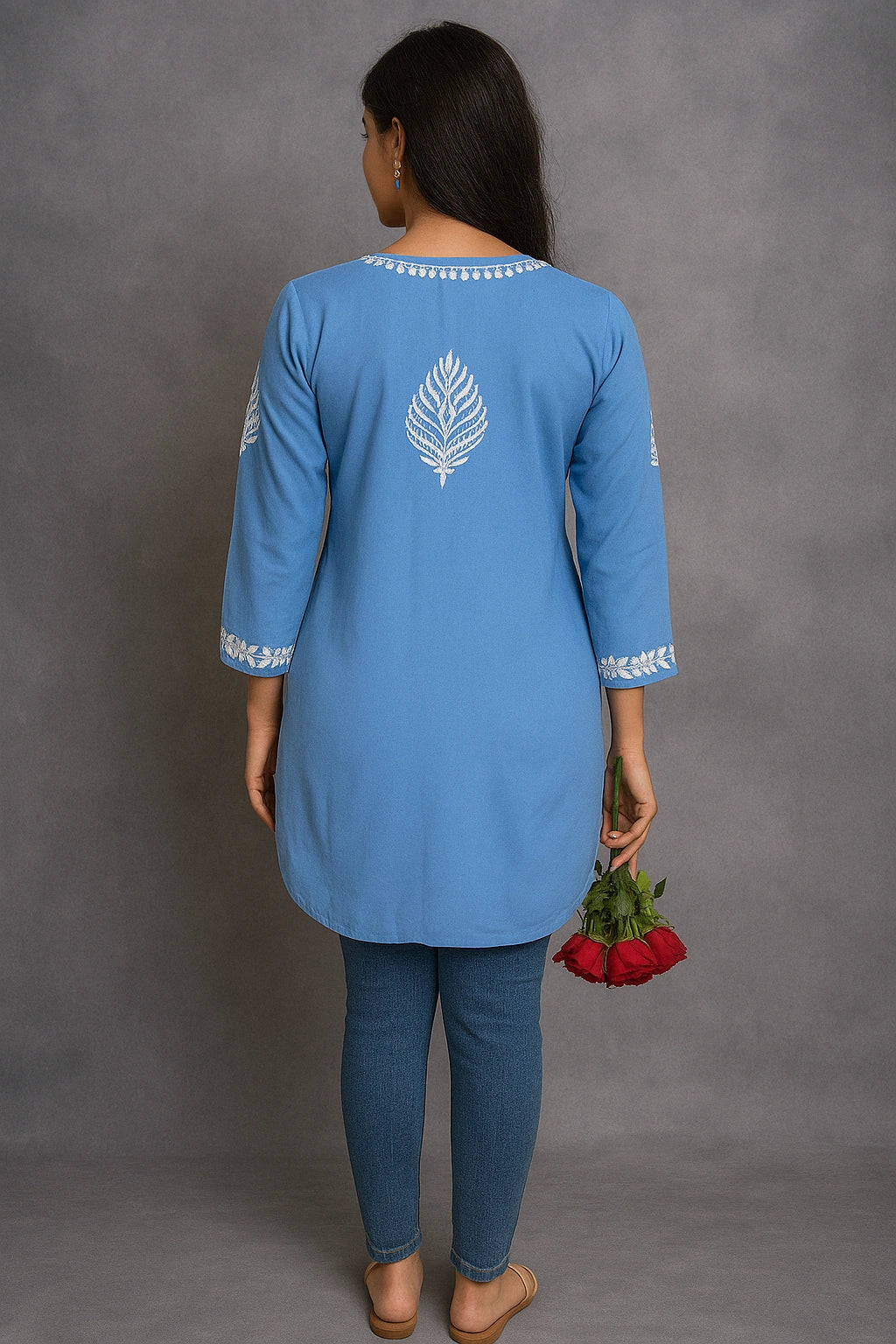 Woman wearing a lucknowi chikankari blue top with white polka dots and blue jeans on a gray background