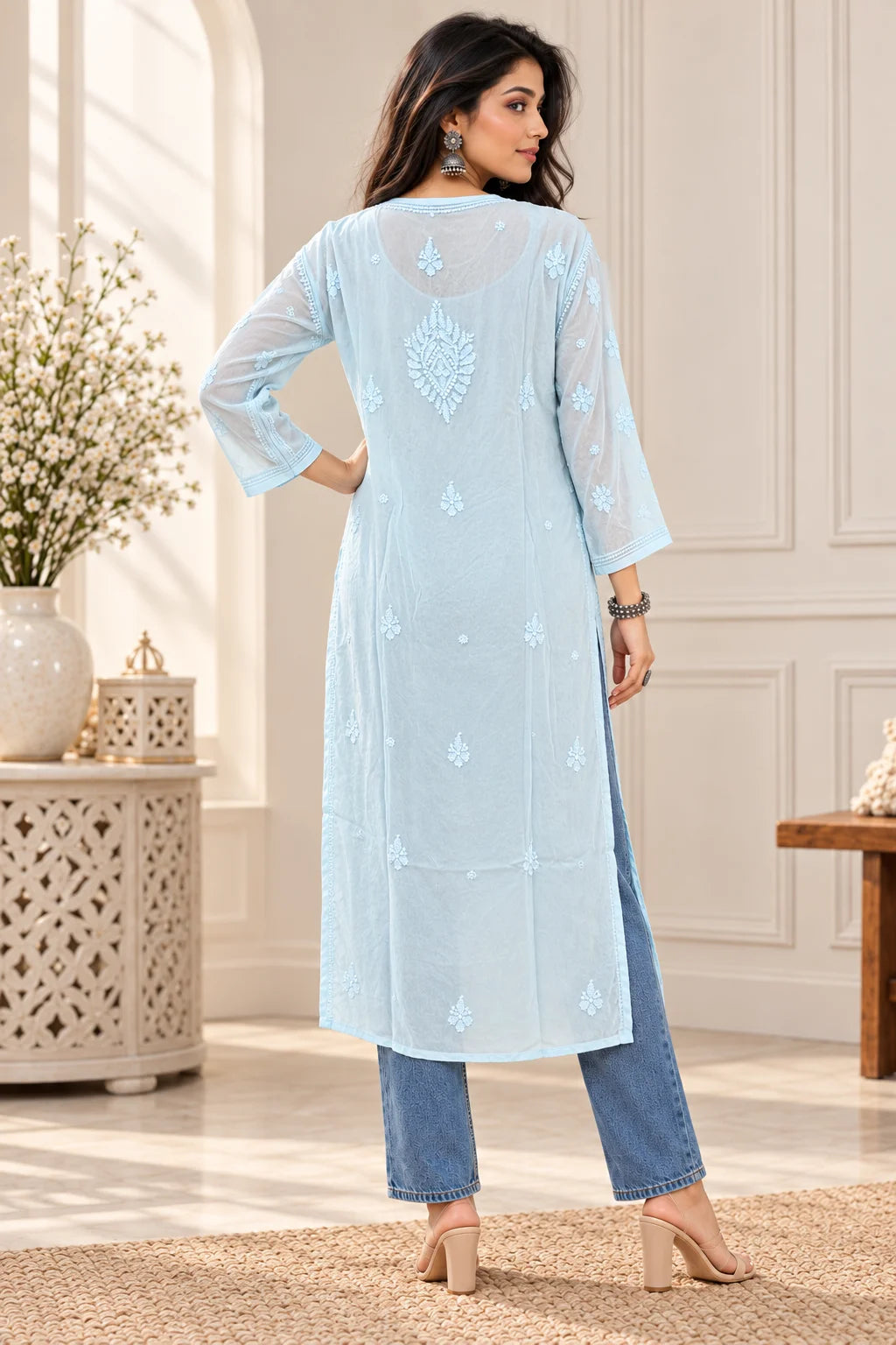 A woman modeling a light blue embroidered kurta from the back, paired with blue jeans and beige heels, standing in a bright, neutral indoor room.