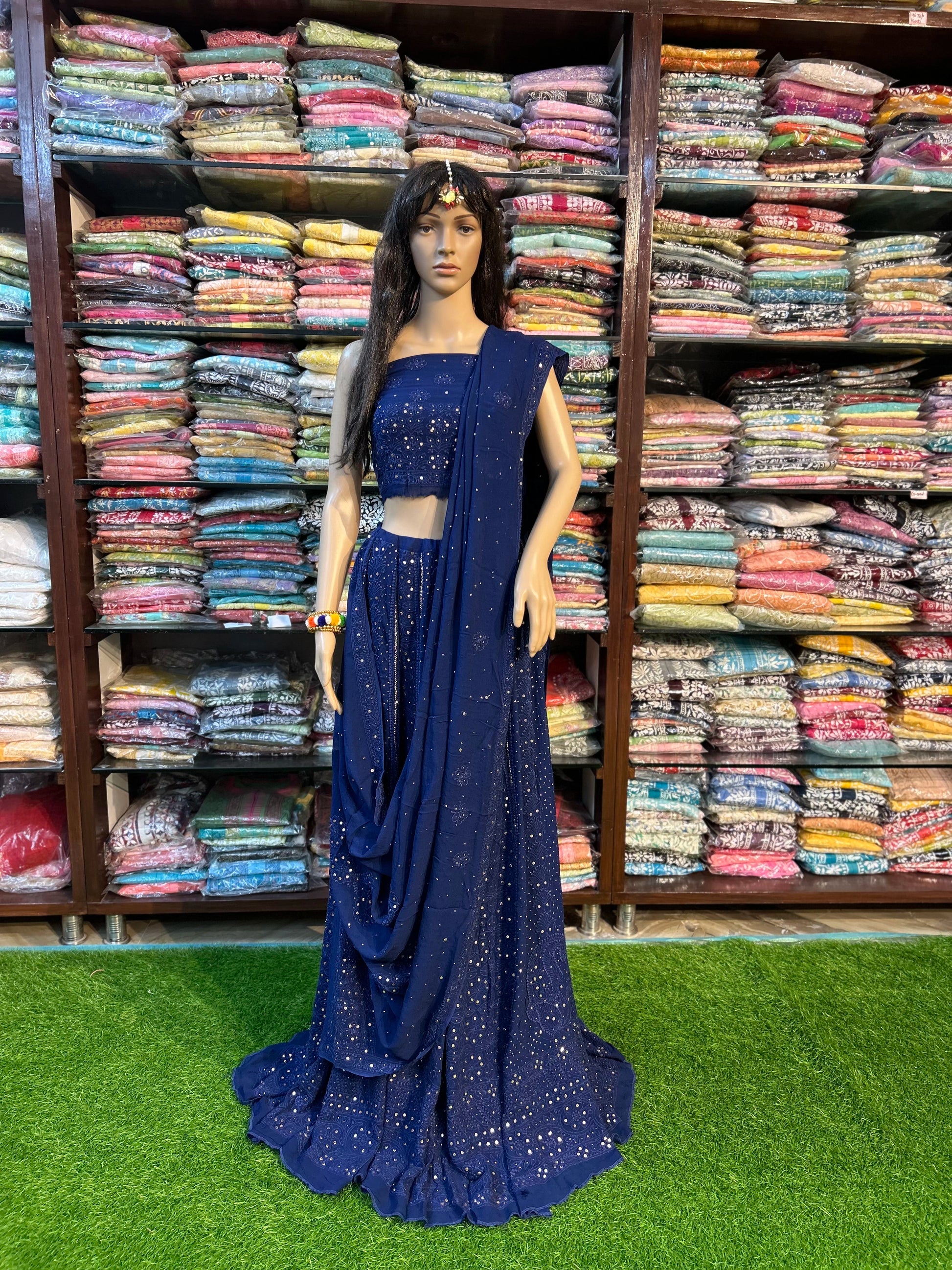 Mannequin wearing a blue saree with a background of stacked fabric rolls.