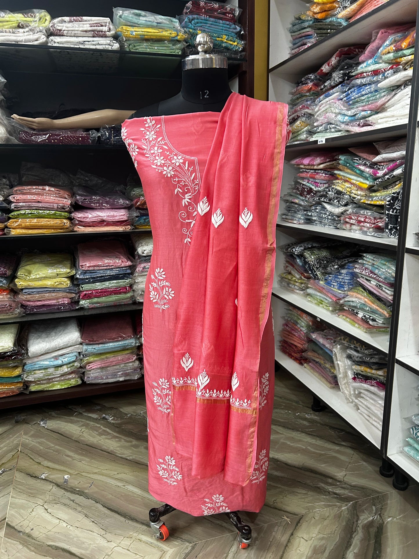 Pink embroidered dress with white patterns on a mannequin in a fabric store.