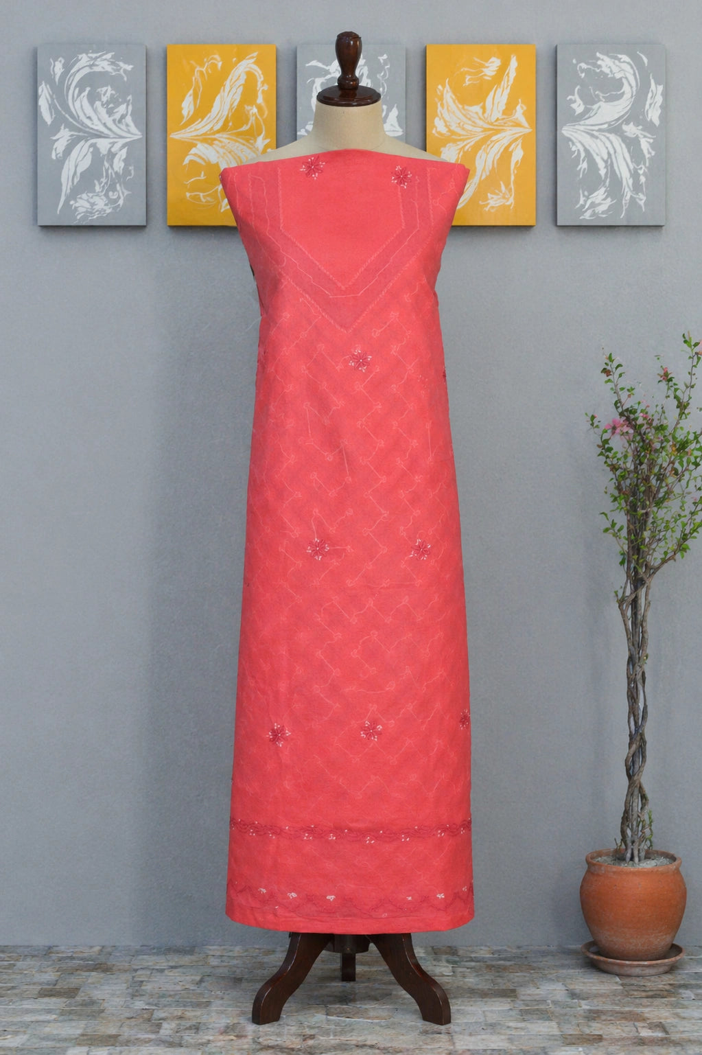 Red embroidered dress on a mannequin against a gray wall with decorative panels.
