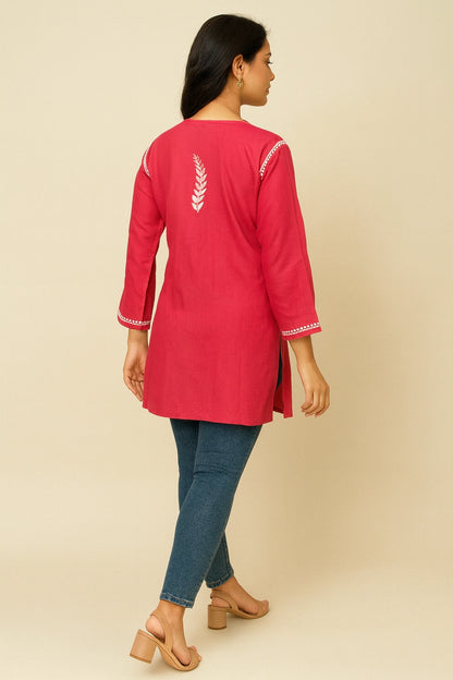 Woman wearing a red embroidered kurta with blue jeans on a beige background
