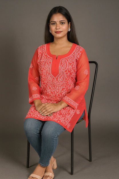 Woman wearing a red embroidered kurta sitting on a chair against a gray background