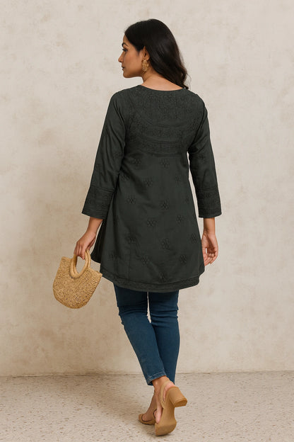 lucknowi chikankari Woman wearing a dark green jacket and blue jeans, holding a woven bag against a beige background