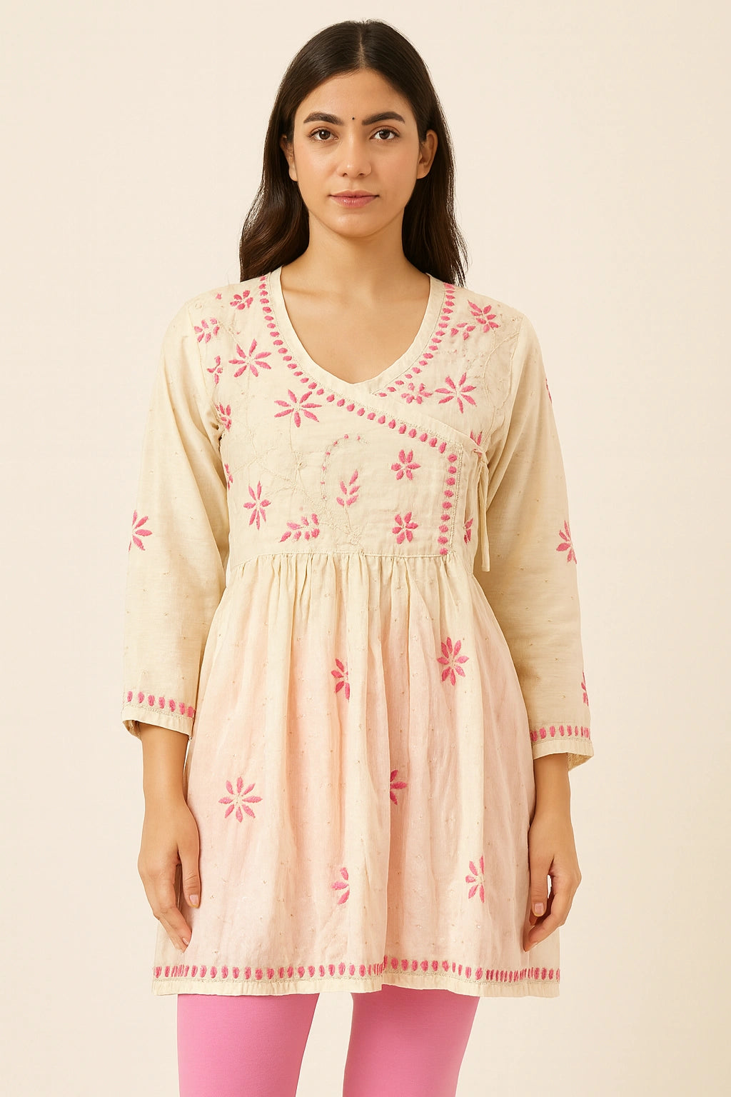 Woman wearing a beige embroidered dress with pink accents on a beige background