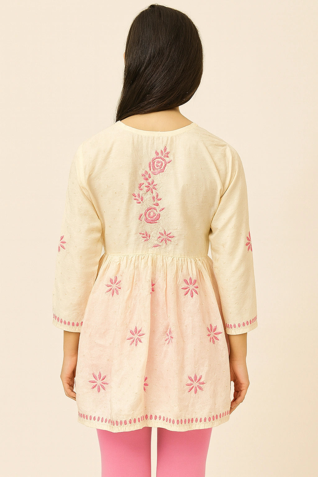 Woman wearing a cream-colored embroidered dress with pink floral patterns on a beige background