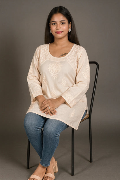 lucknowi chikankari Woman sitting on a chair wearing a beige top and blue jeans against a gray background