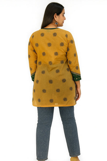 Woman wearing a lucknowi chikankari mustard yellow kurta with black patterns and blue jeans on a white background