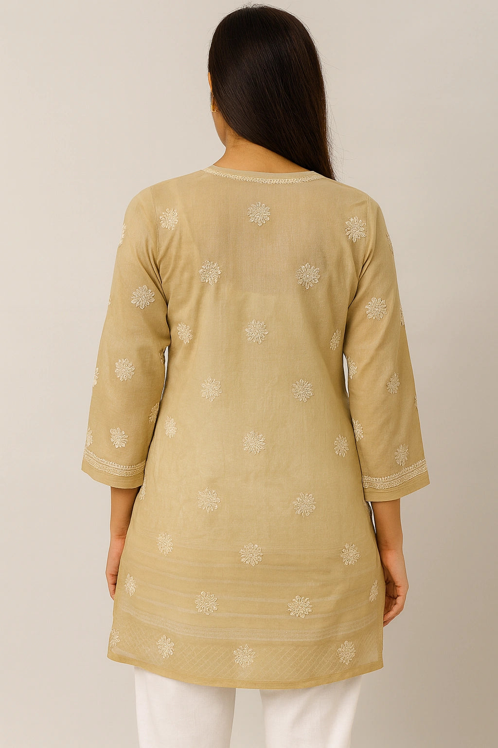 Woman wearing a beige embroidered top and white pants on a plain background