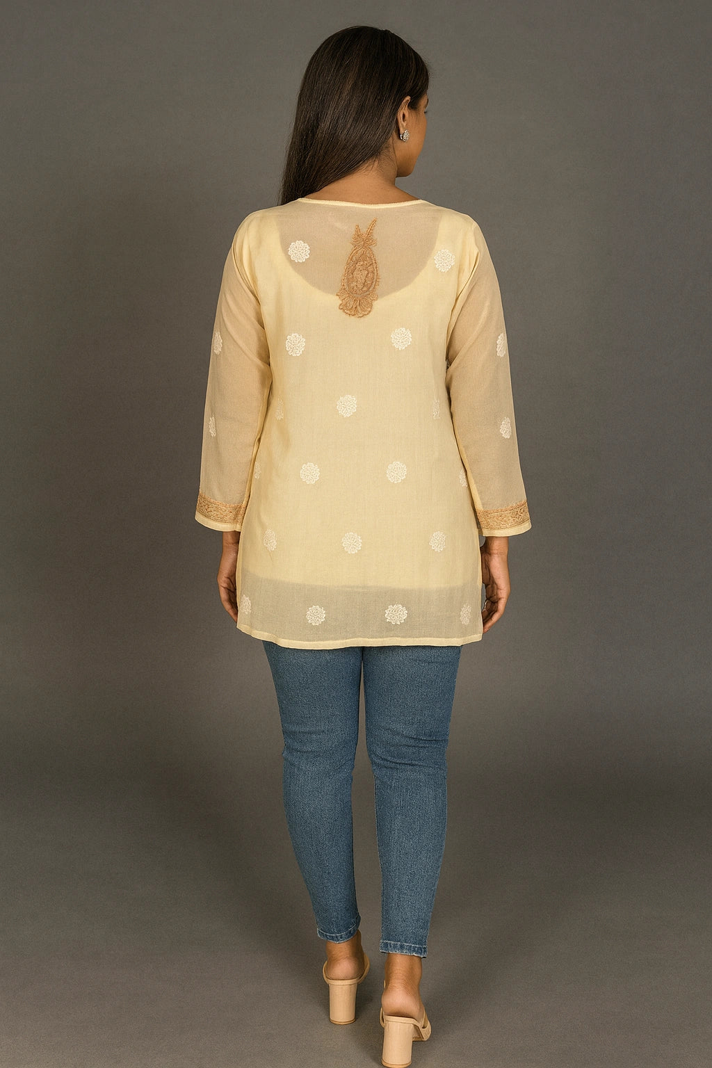 Woman wearing a lucknowi chikankari beige top with white polka dots and blue jeans on a gray background
