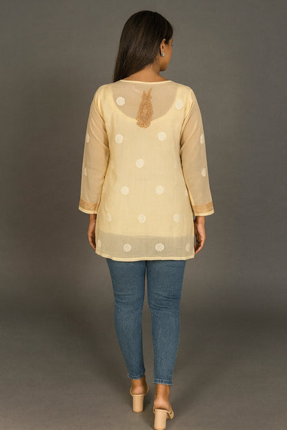 Woman wearing a lucknowi chikankari beige top with white polka dots and blue jeans on a gray background