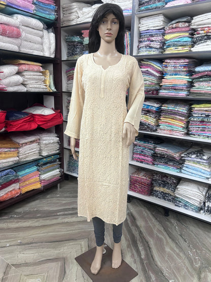 A beige long-sleeve kurta with a textured floral pattern, displayed on a female mannequin in a clothing store. The mannequin is also wearing dark gray leggings, and the background features shelves packed with folded colorful garments.
