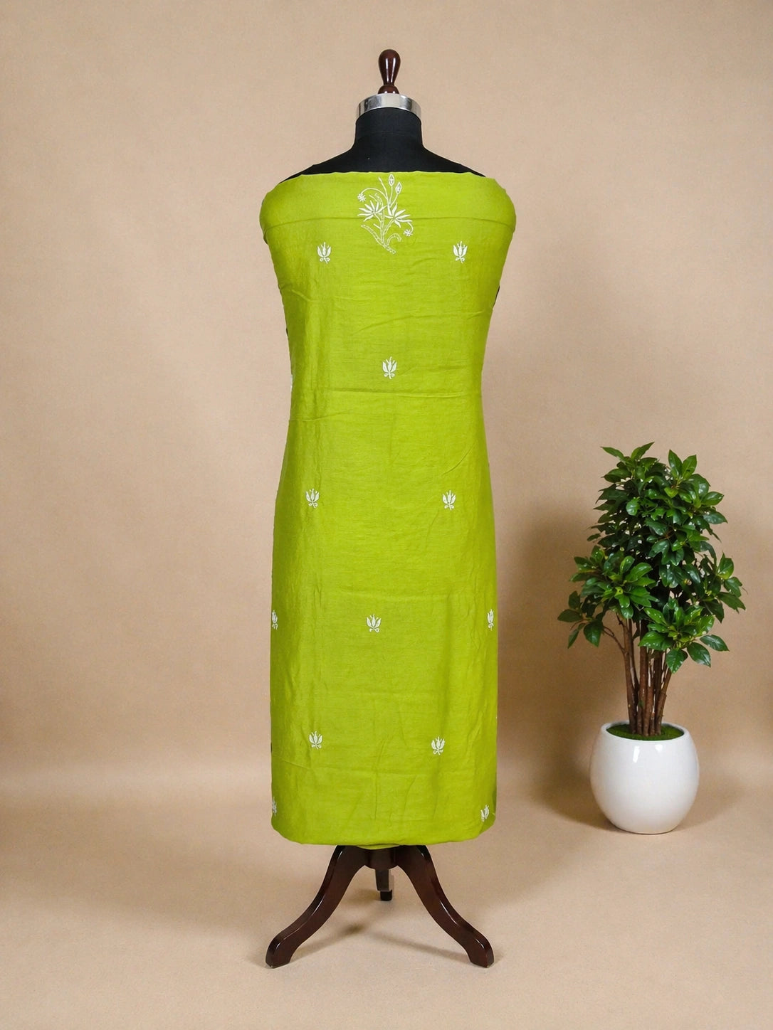 Green embroidered dress on a mannequin with a plant in the background