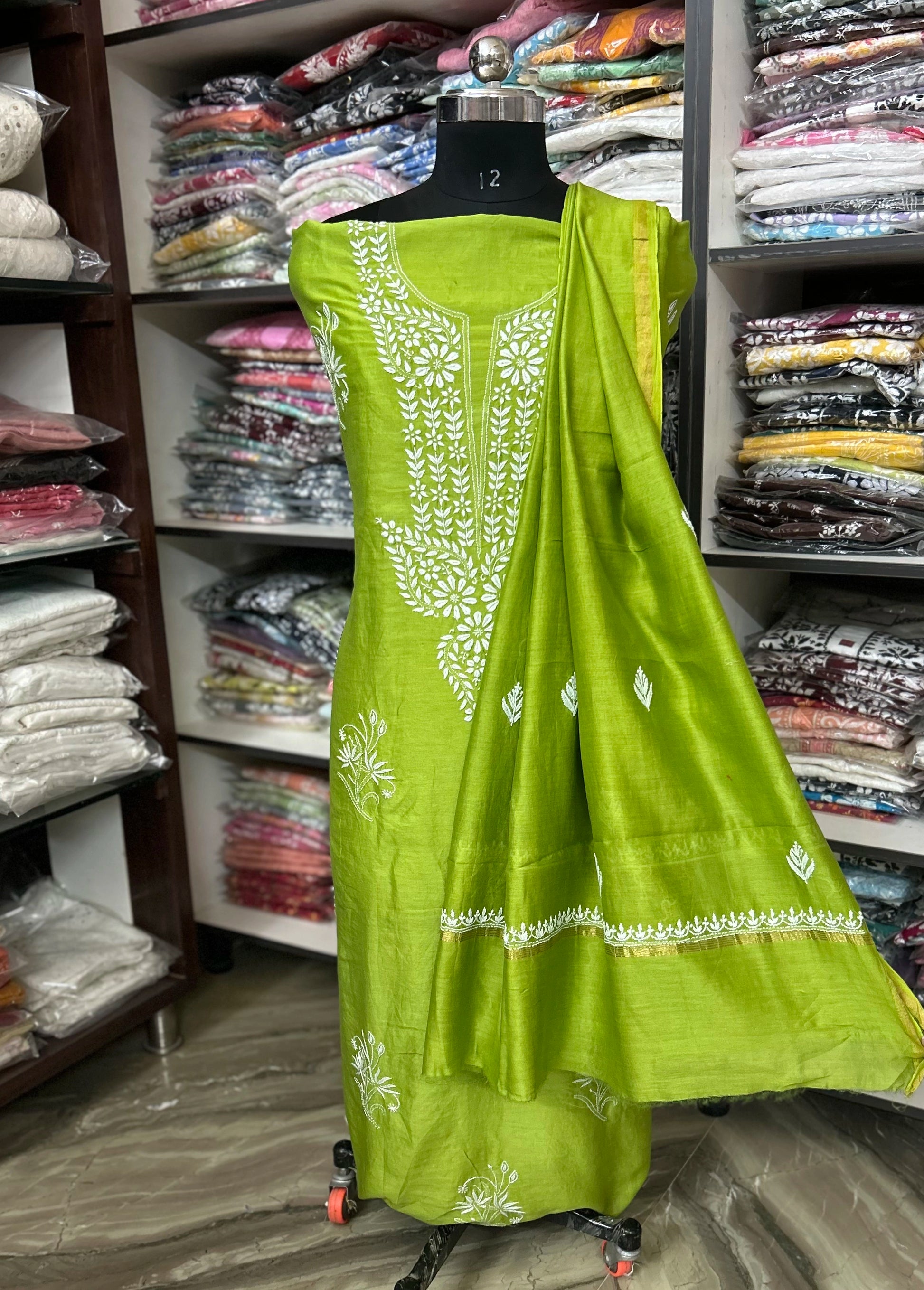 Green saree with white embroidery on a mannequin in a clothing store.