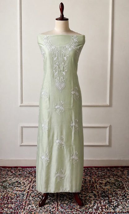 Light green dress with white floral embroidery on a mannequin against a white paneled wall.