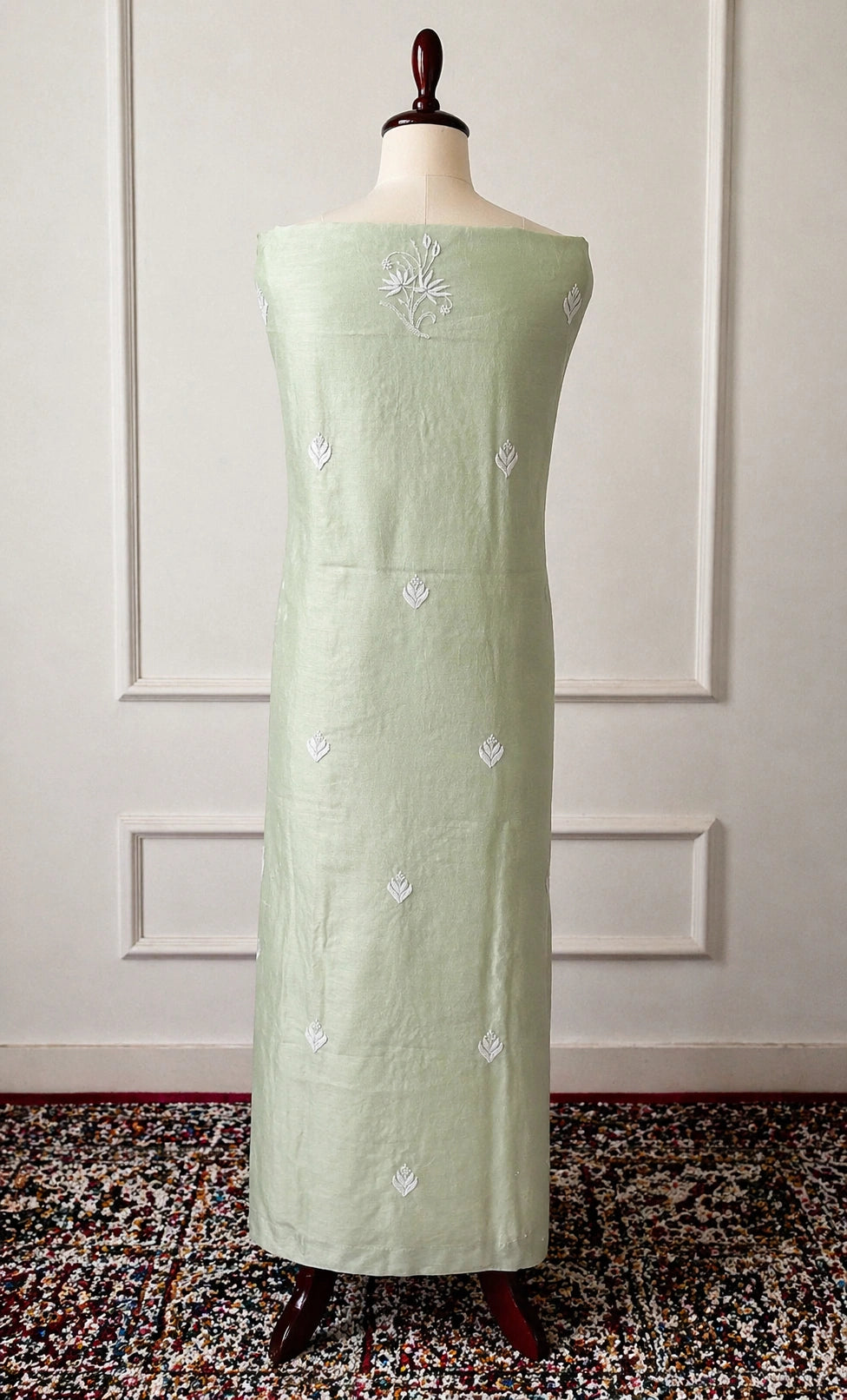 Light green dress with floral embroidery on a mannequin against a white paneled wall.