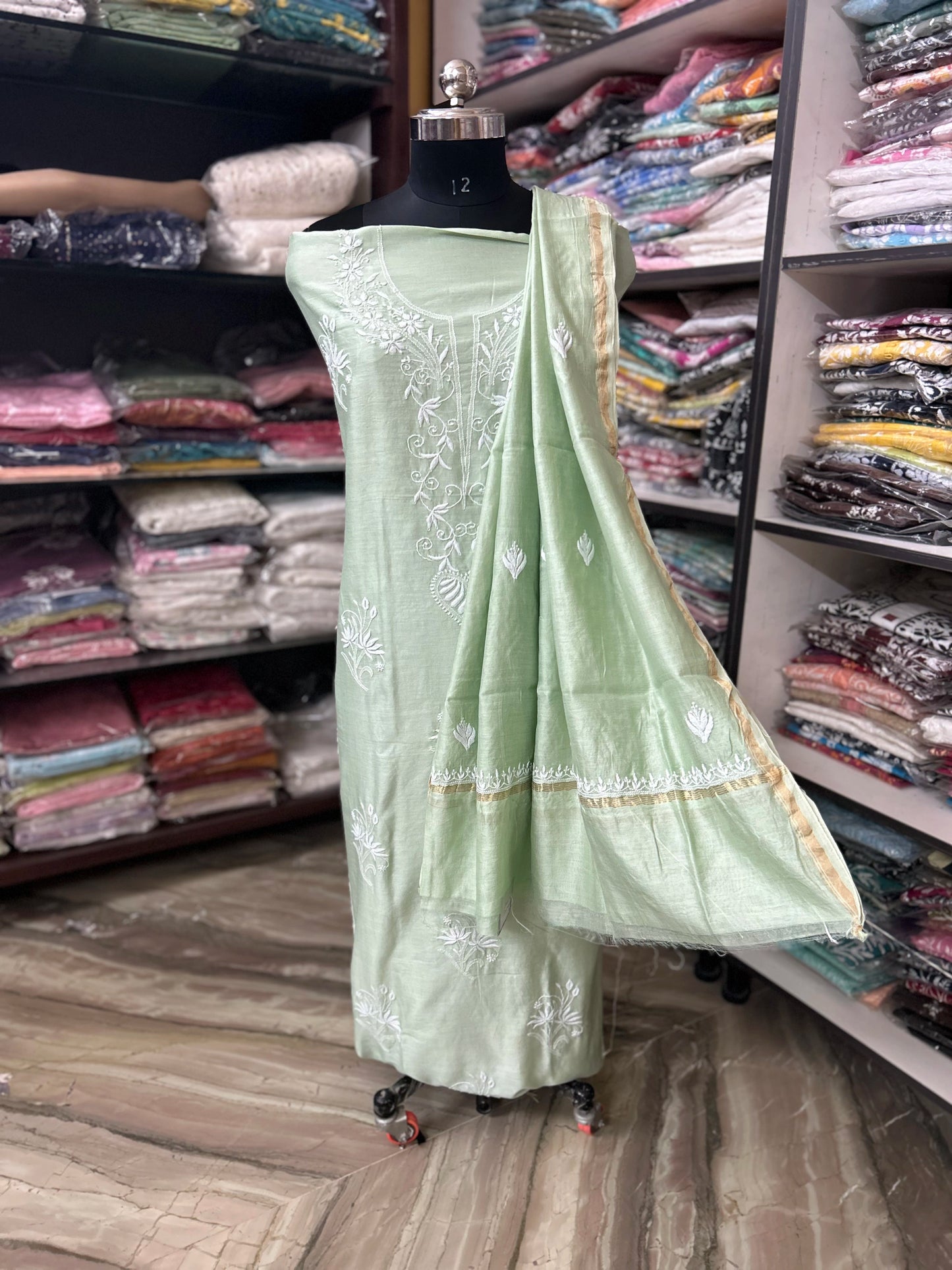 Light green embroidered saree on a mannequin in a fabric store.