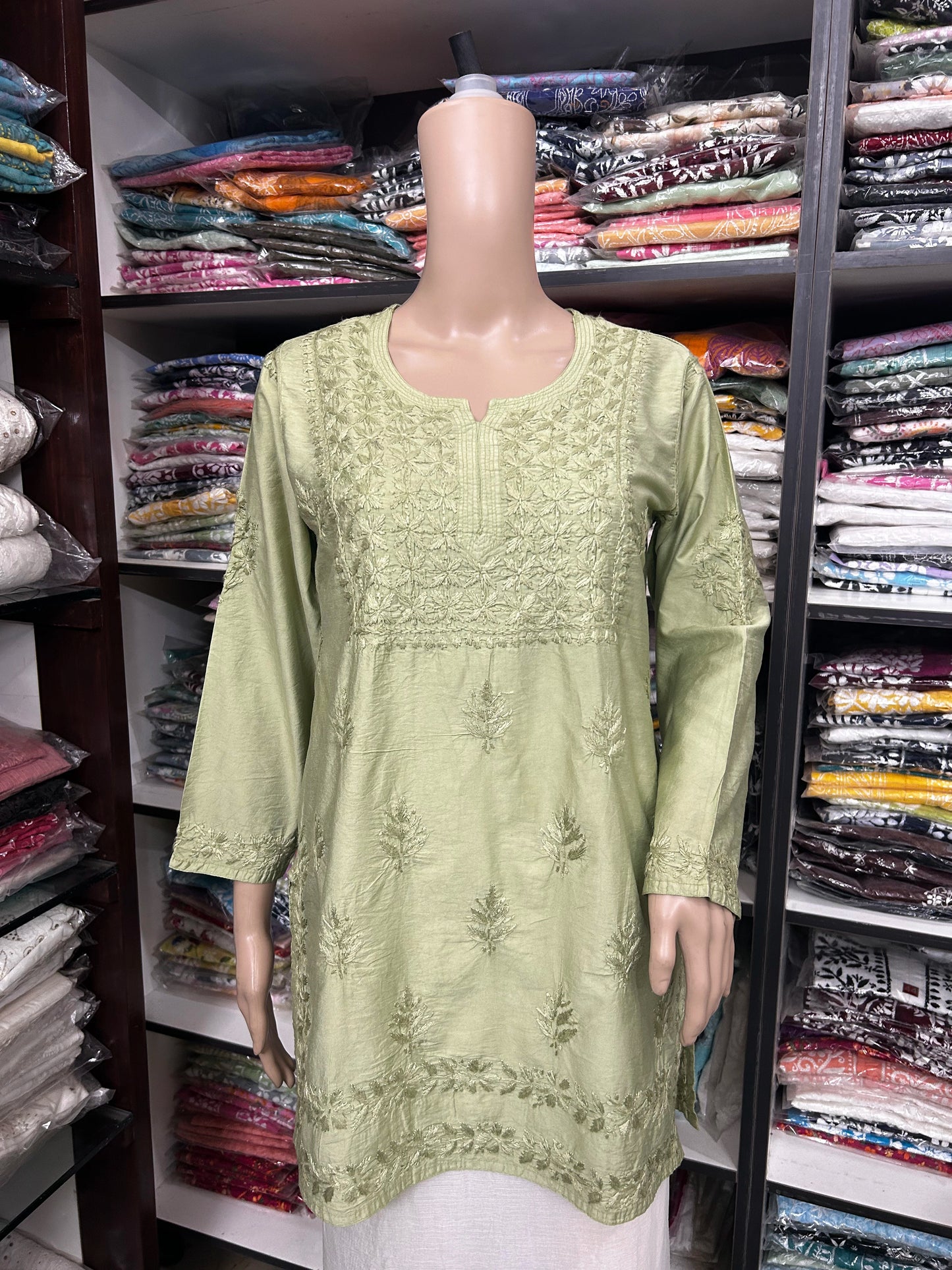 Mannequin wearing a green embroidered dress in a fabric store.