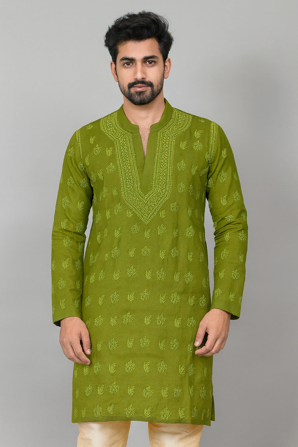 A man wearing a sage green kurta with light green floral embroidery and a split neckline, paired with cream trousers, standing against a solid gray background.