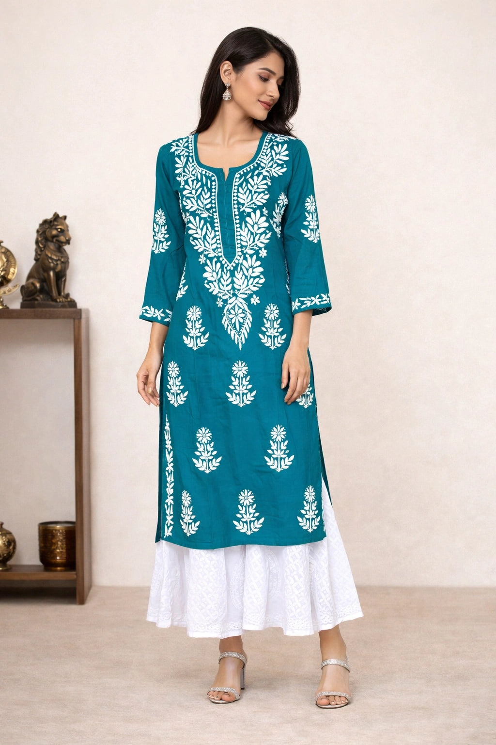 Woman wearing a teal and white embroidered kurta with a white skirt against a neutral background.