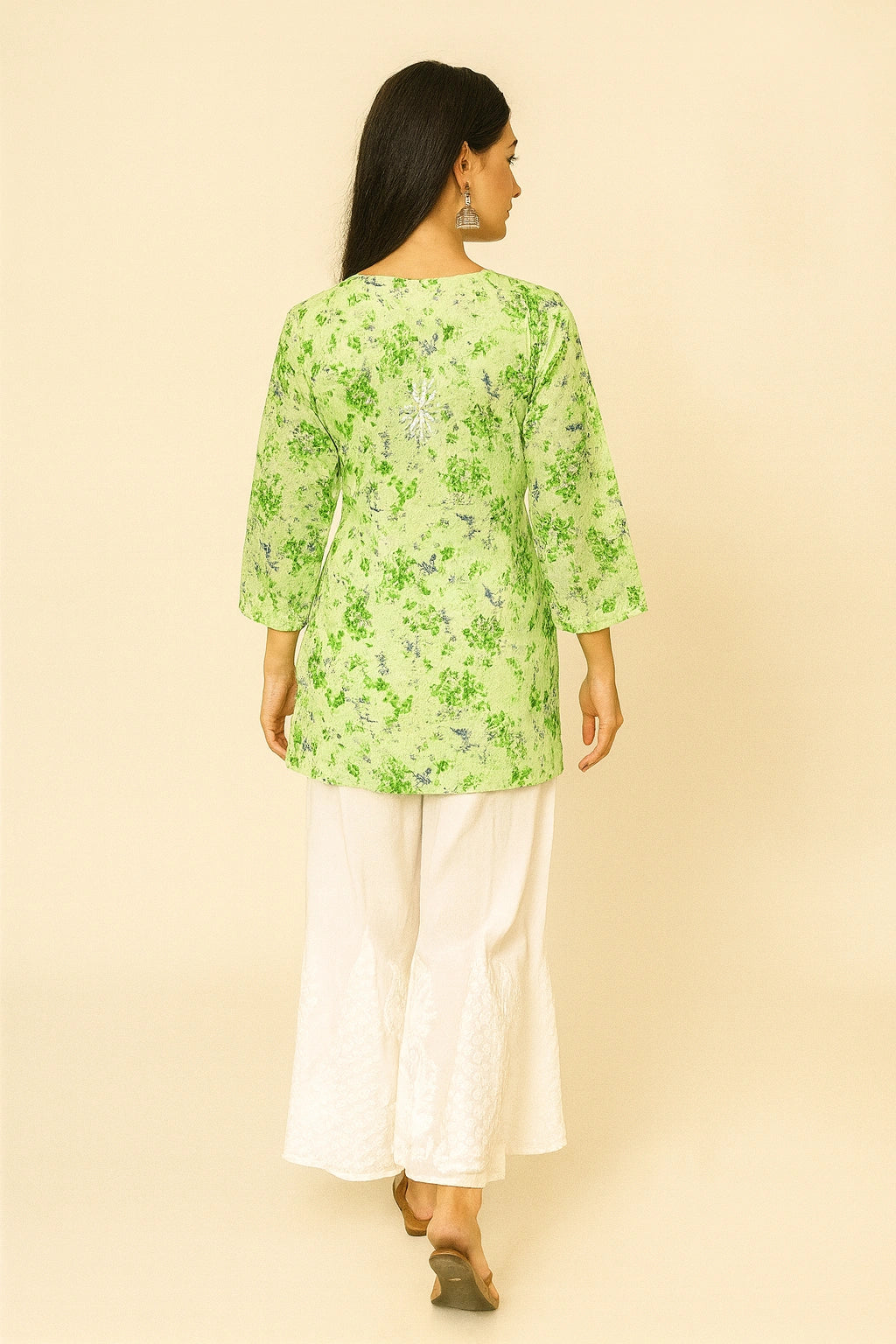 Woman wearing a lucknowi chikankari green floral top and white pants on a beige background
