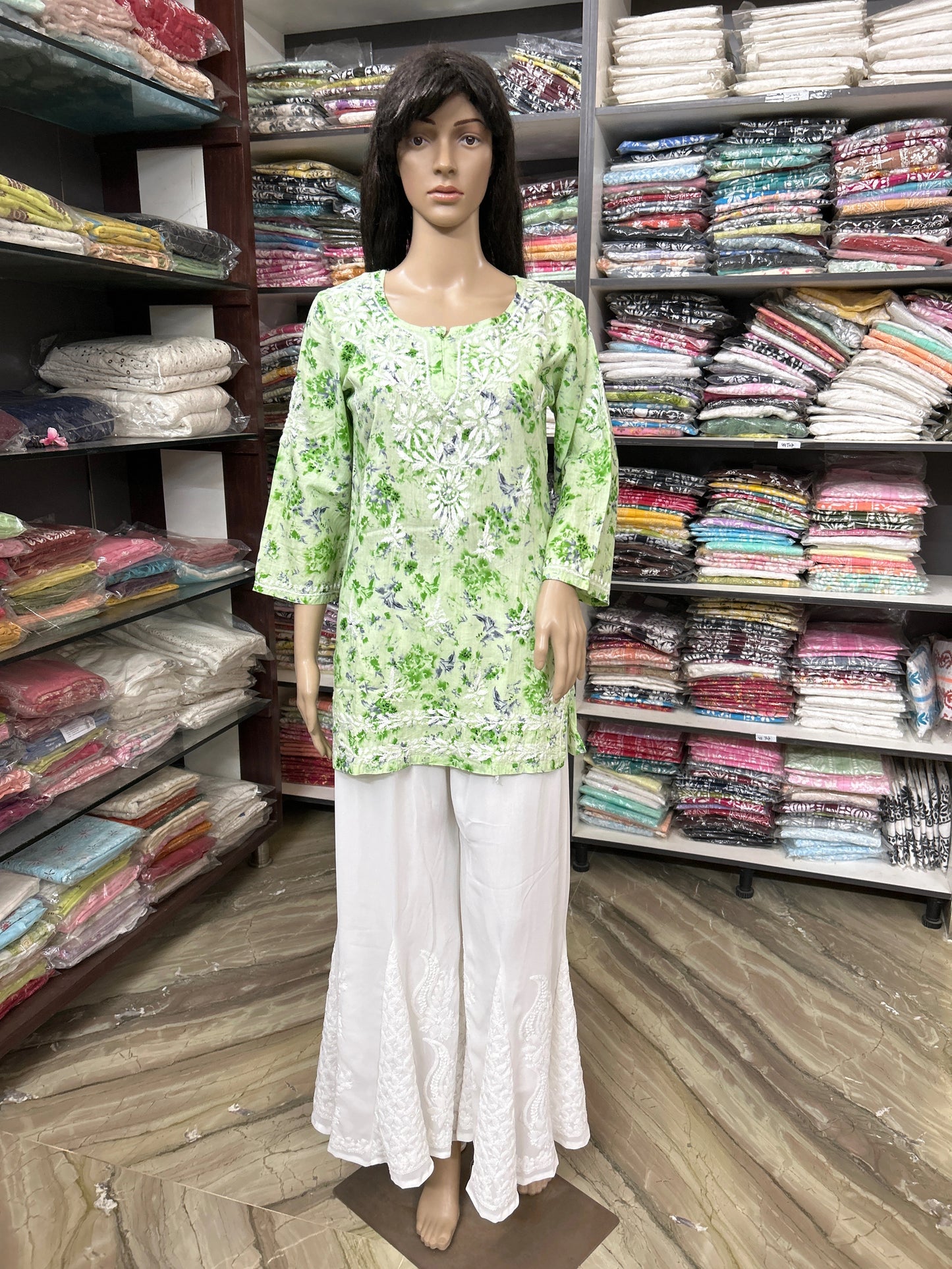Mannequin wearing a lucknowi chikankari green floral top and white pants in a fabric store.