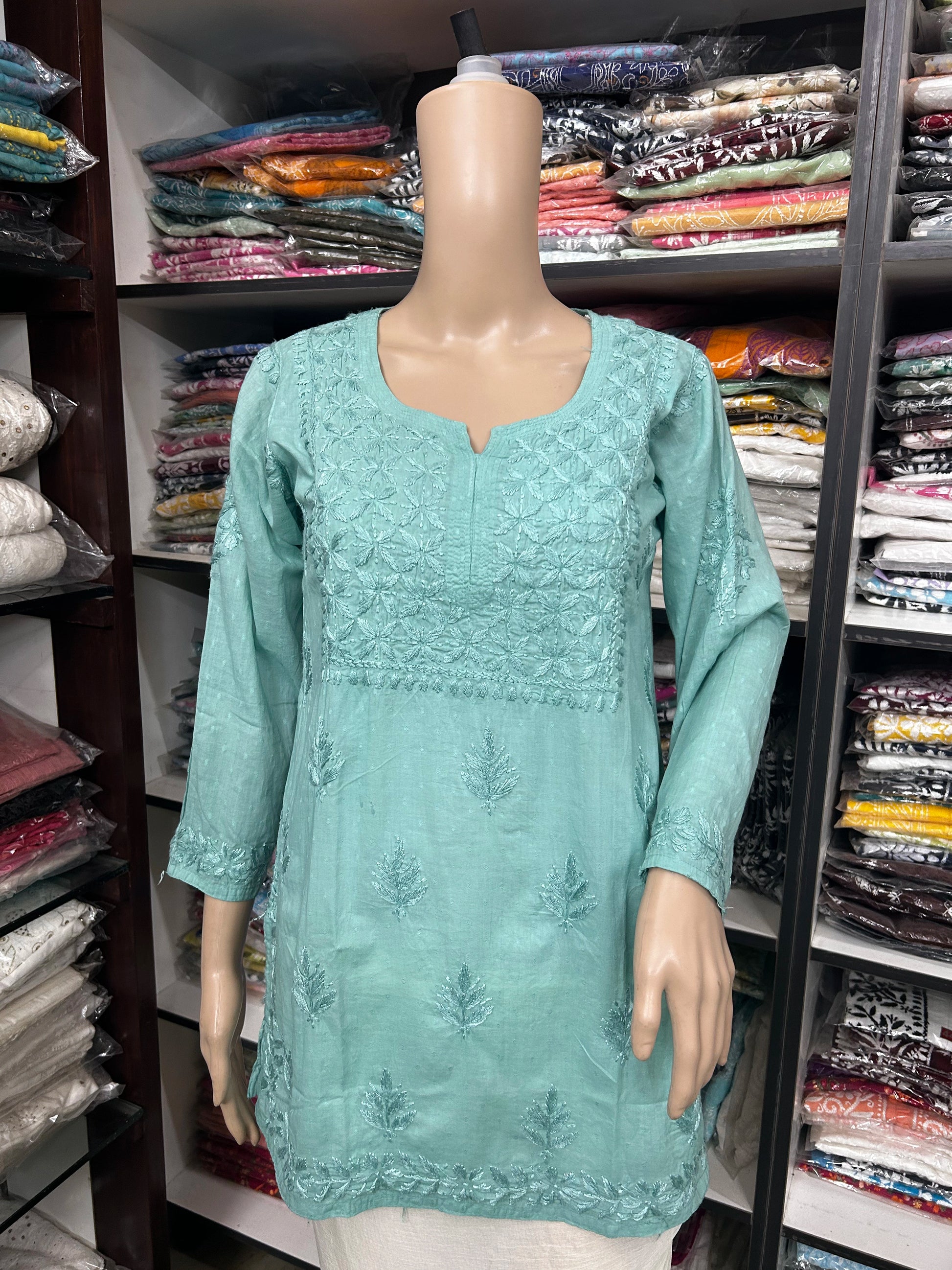 Mannequin wearing a light blue embroidered top in a fabric store.