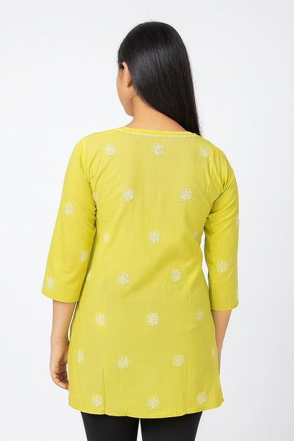 Woman wearing a lucknowi chikankari yellow kurta with white floral patterns on a white background