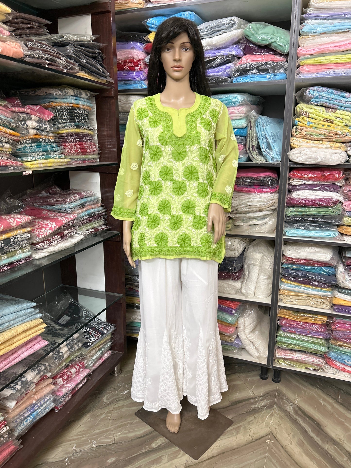 lucknowi chikankari Mannequin wearing a green patterned top and white pants in a fabric store.