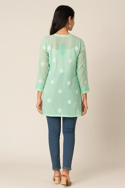 Woman wearing a green embroidered top with white polka dots on a gray background