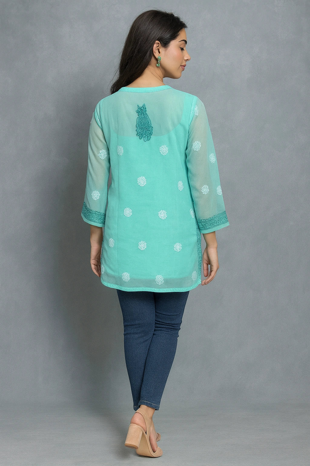 Woman wearing a light blue embroidered top with white polka dots on a gray background