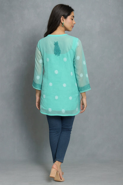Woman wearing a light blue embroidered top with white polka dots on a gray background