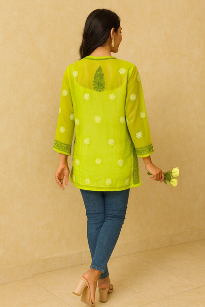 Woman wearing a green embroidered top with white polka dots on a gray background