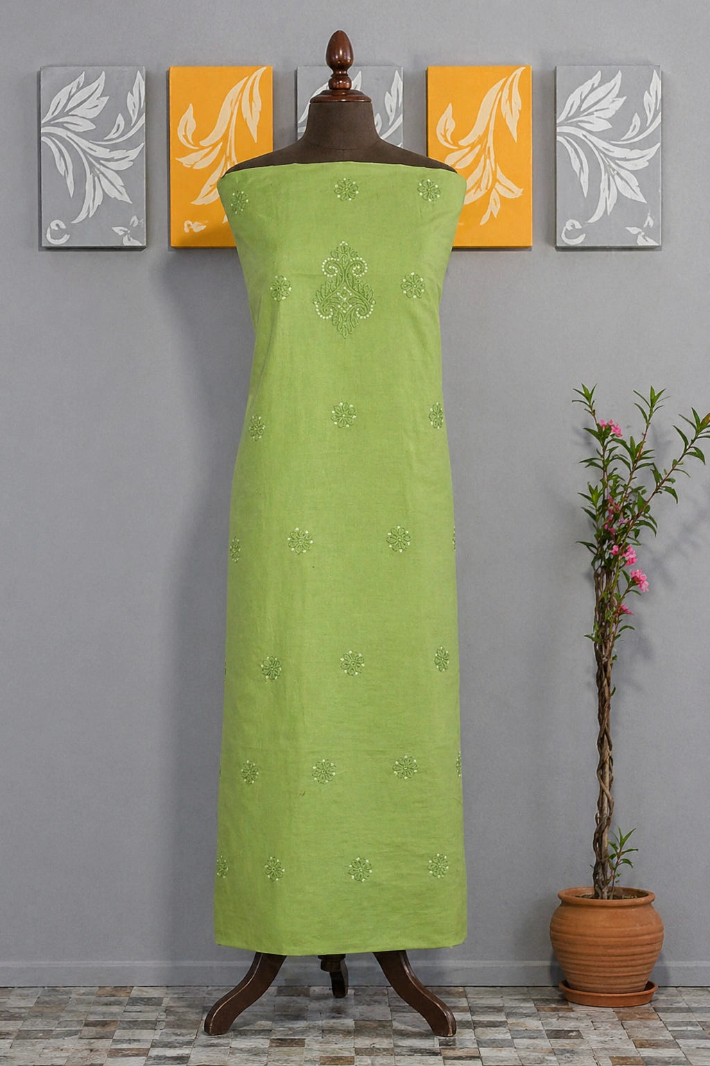 Green dress on a mannequin against a gray wall with decorative panels and a plant.