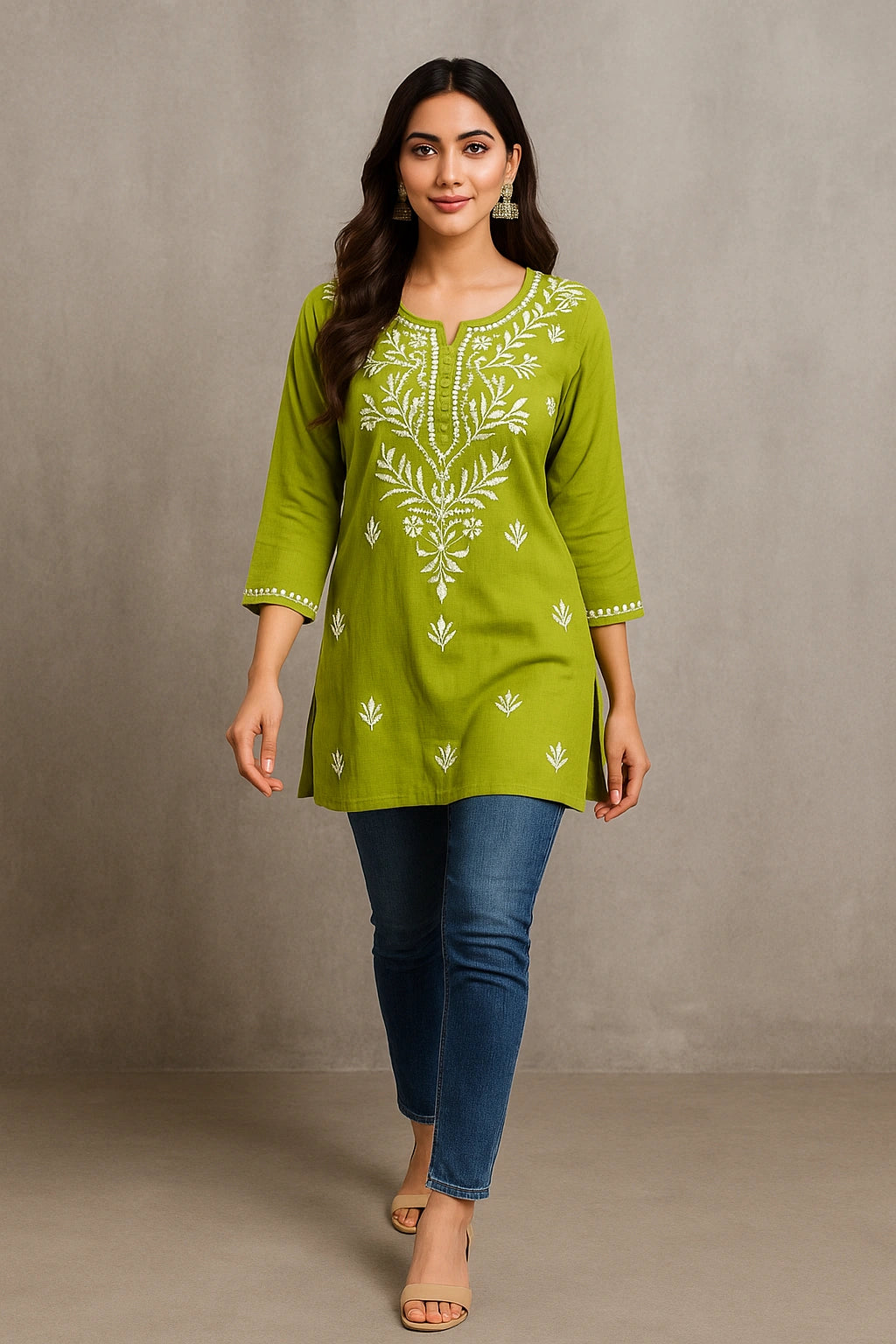 Woman wearing a green embroidered top and blue jeans against a gray background