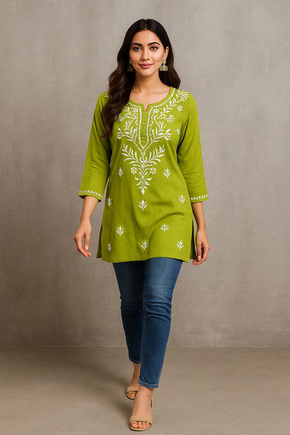 Woman wearing a green embroidered top and blue jeans against a gray background