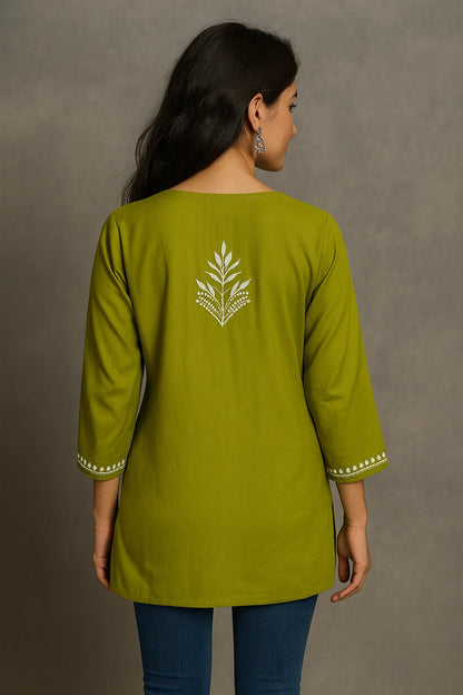 Woman wearing a green embroidered top against a gray background