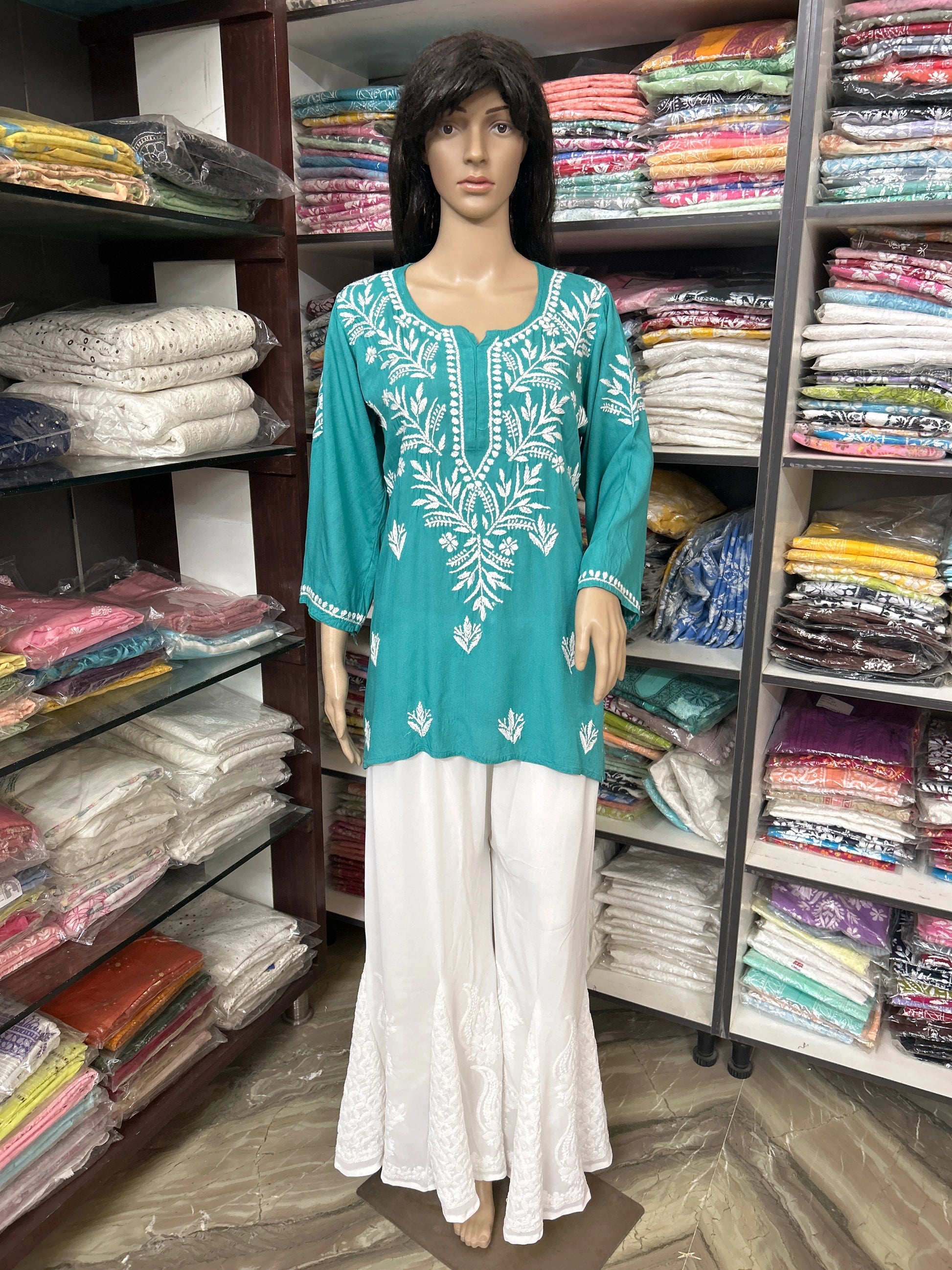 Mannequin wearing a teal embroidered top and white pants in a fabric store.