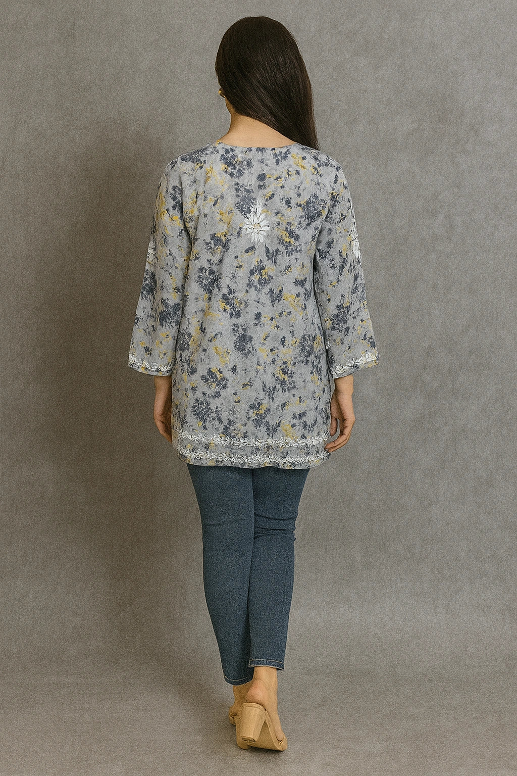 Woman wearing a lucknowi chikankari floral blouse and jeans against a gray background