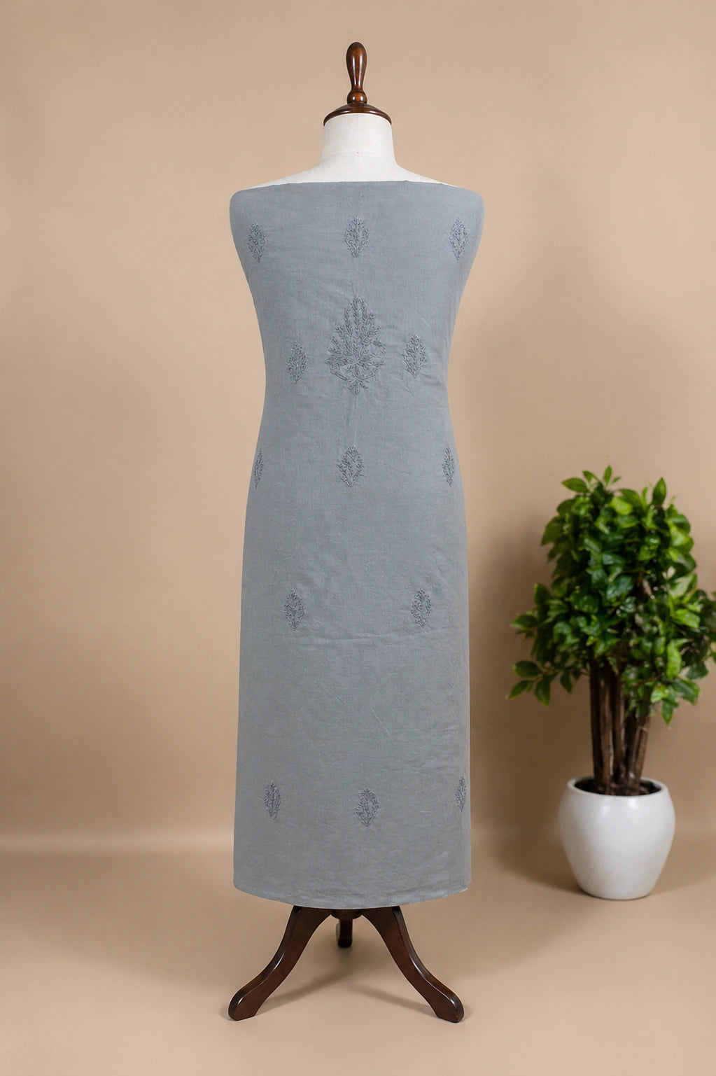 Gray dress on a mannequin with a beige background and a potted plant.