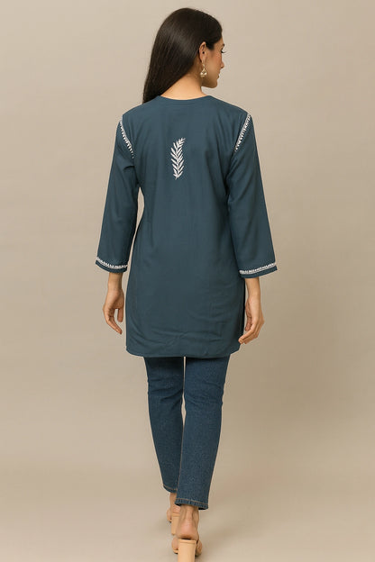 Woman wearing a teal kurta with white embroidery on a beige background