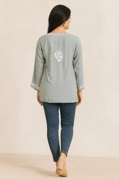 Woman wearing a light gray embroidered top and blue jeans on a beige background