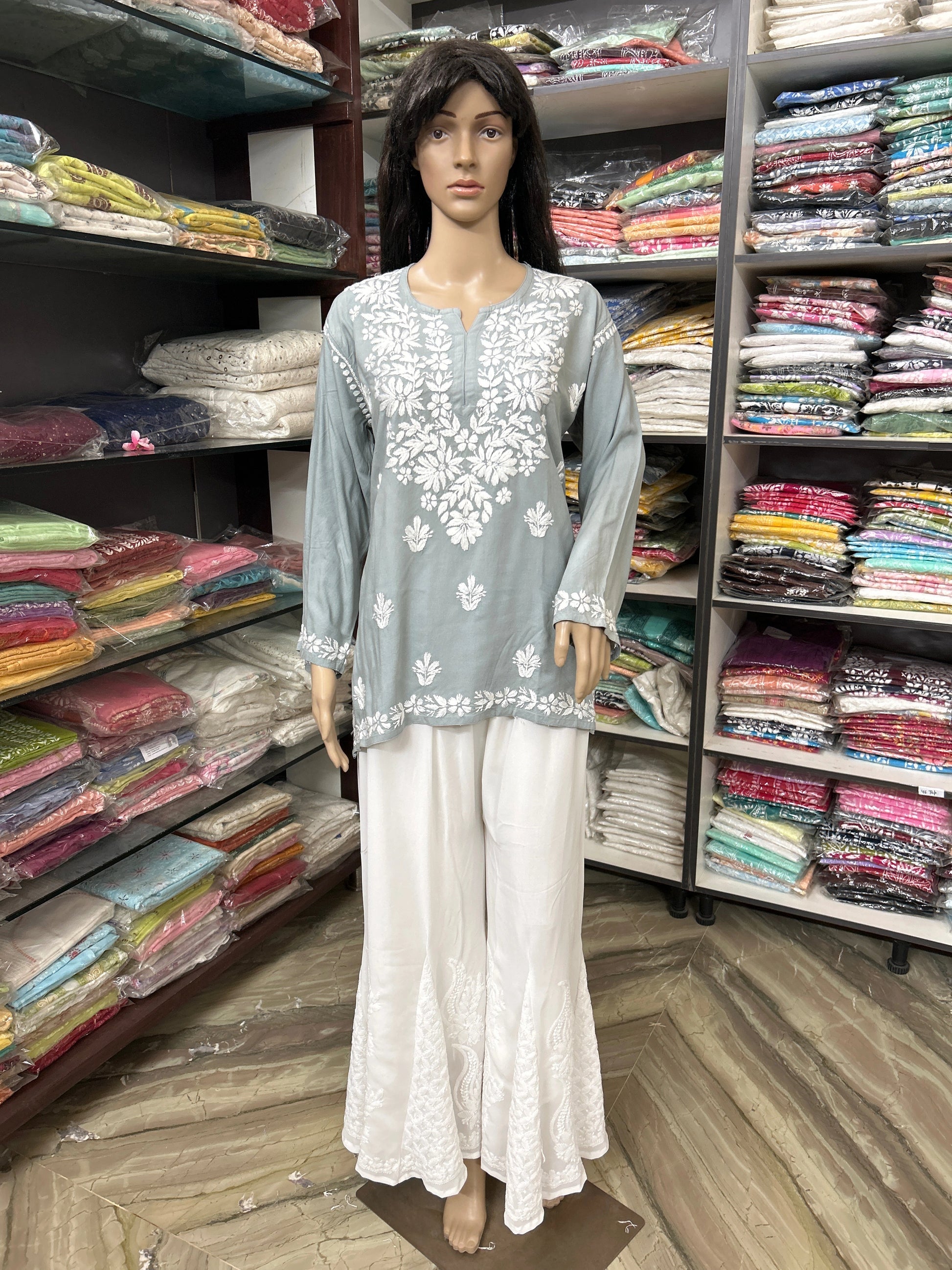 Mannequin wearing a light blue embroidered top and white pants in a fabric store.