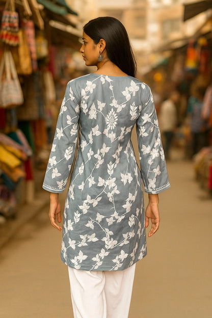 Woman wearing a lucknowi chikankari grey top with white polka dots and blue jeans on a gray background